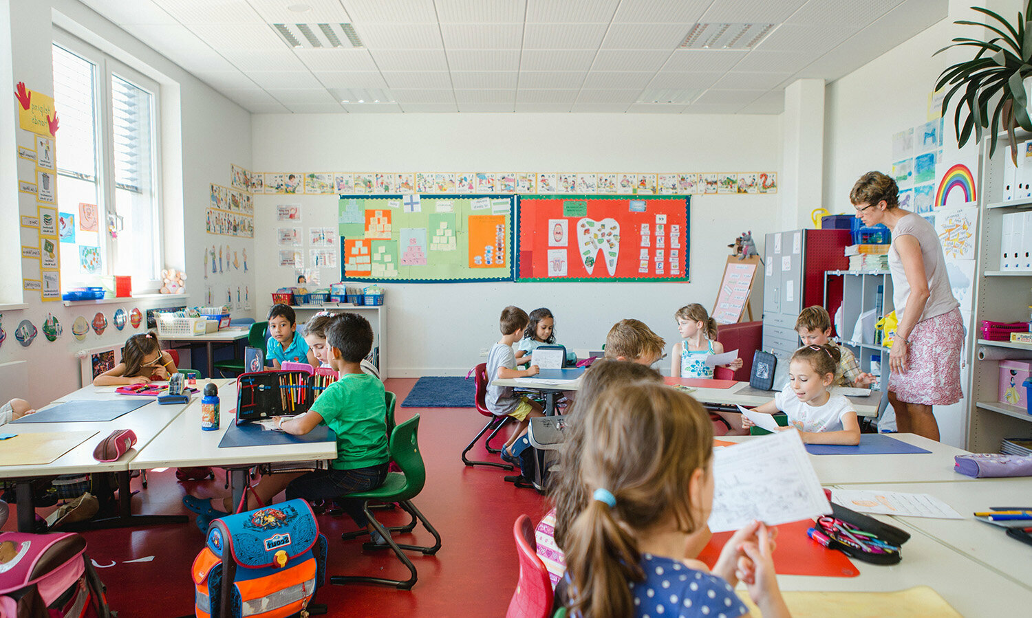 Primary school students sit at their desks in a colourful classroom and work.