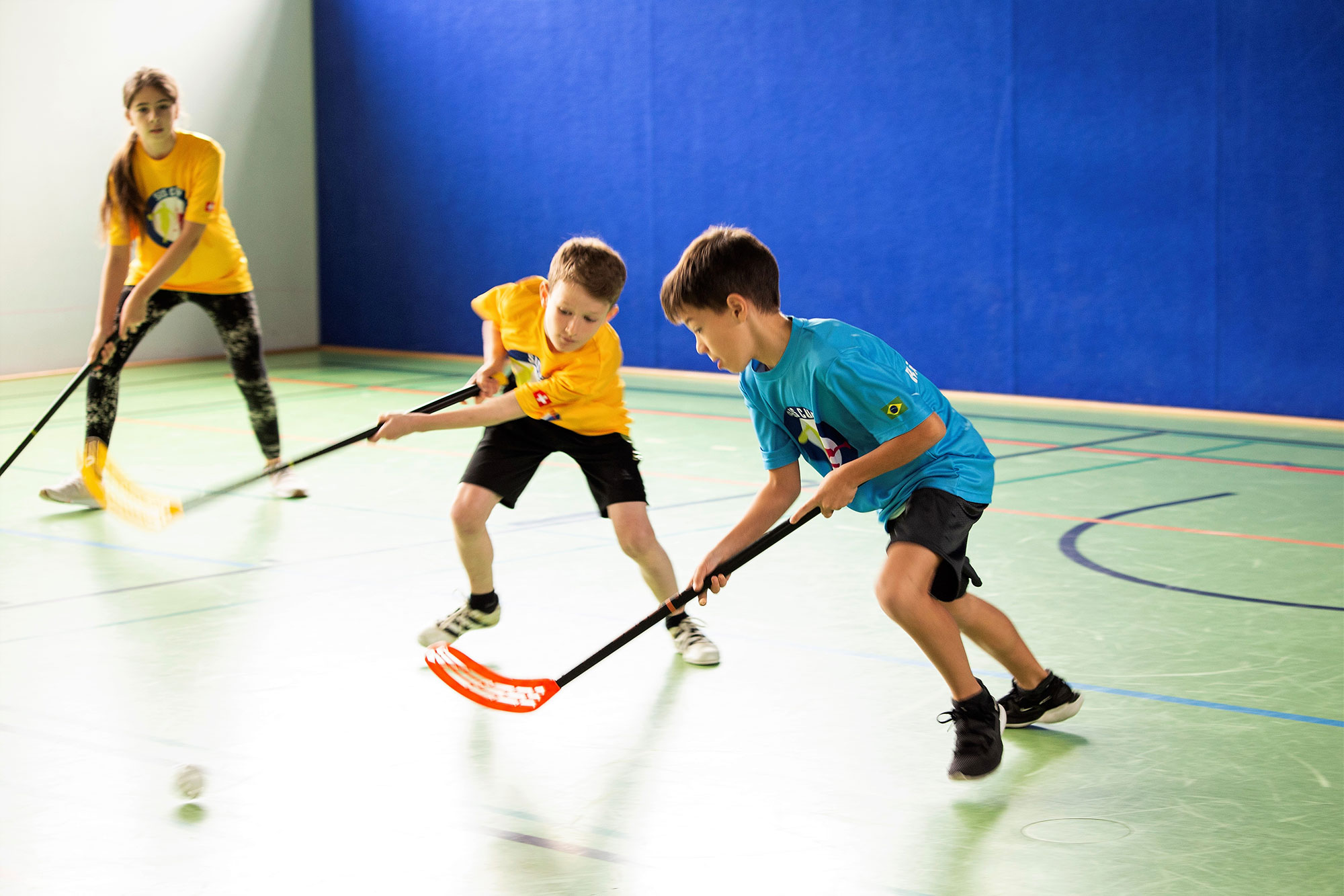 Two boys fighting for the ball in floorball in a gym. 